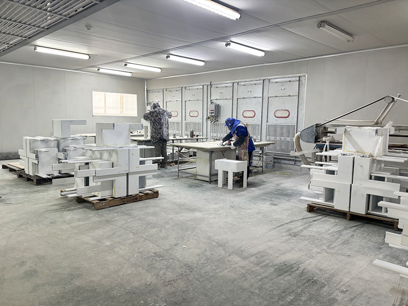 Professional painting and finishing booth in Hyman Hospitality facility, showing operators applying coatings to custom furniture pieces.
