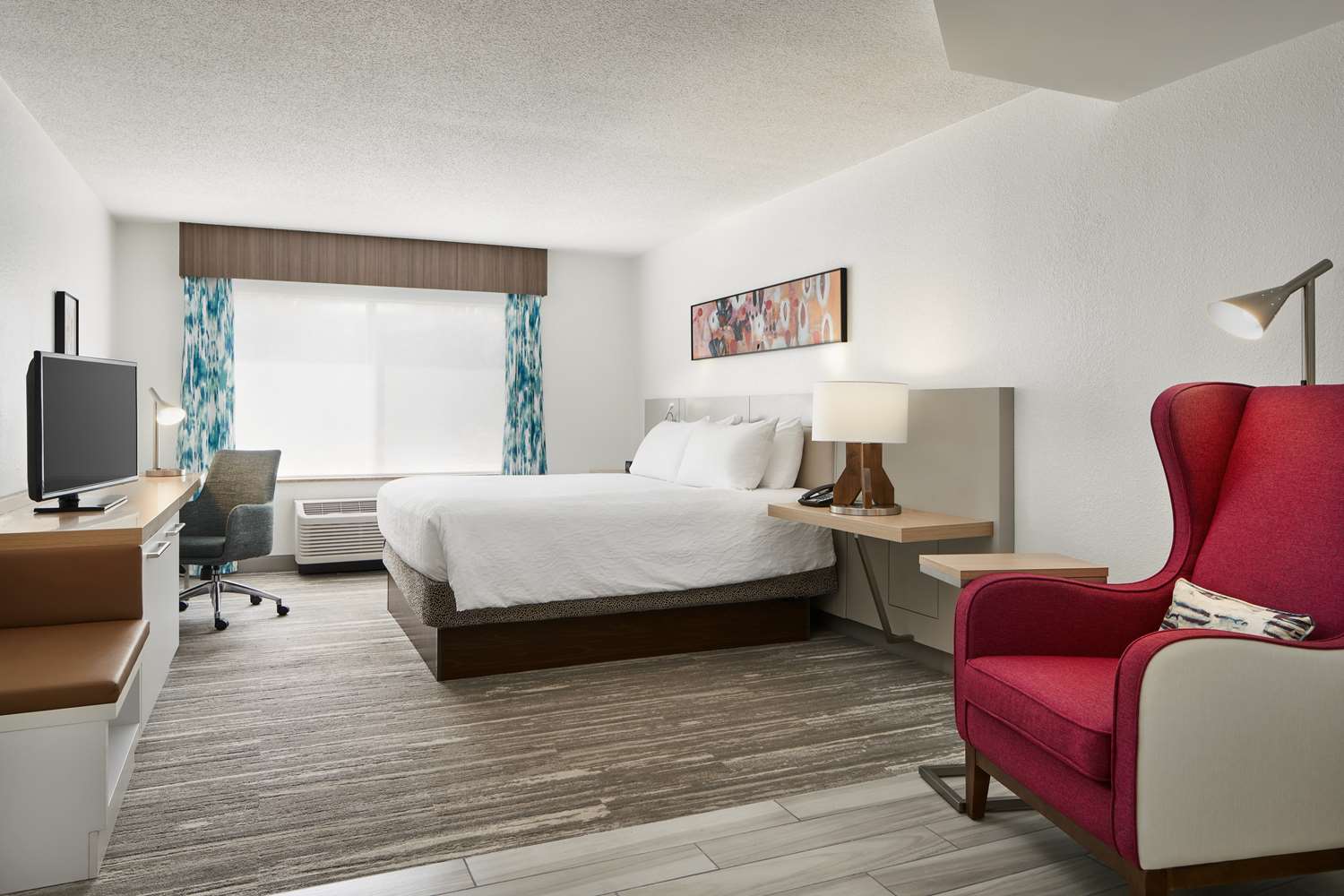 Full guestroom interior for Hilton brand hotels featuring the GR-101 red wingback lounge chair, integrated Studio Teak nightstands, and a custom media desk for PIP renovations.