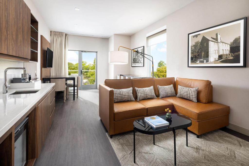 Upscale hotel suite interior for AC Hotels featuring a cognac leather sectional sofa and integrated kitchenette cabinetry with stone-integrated tops.