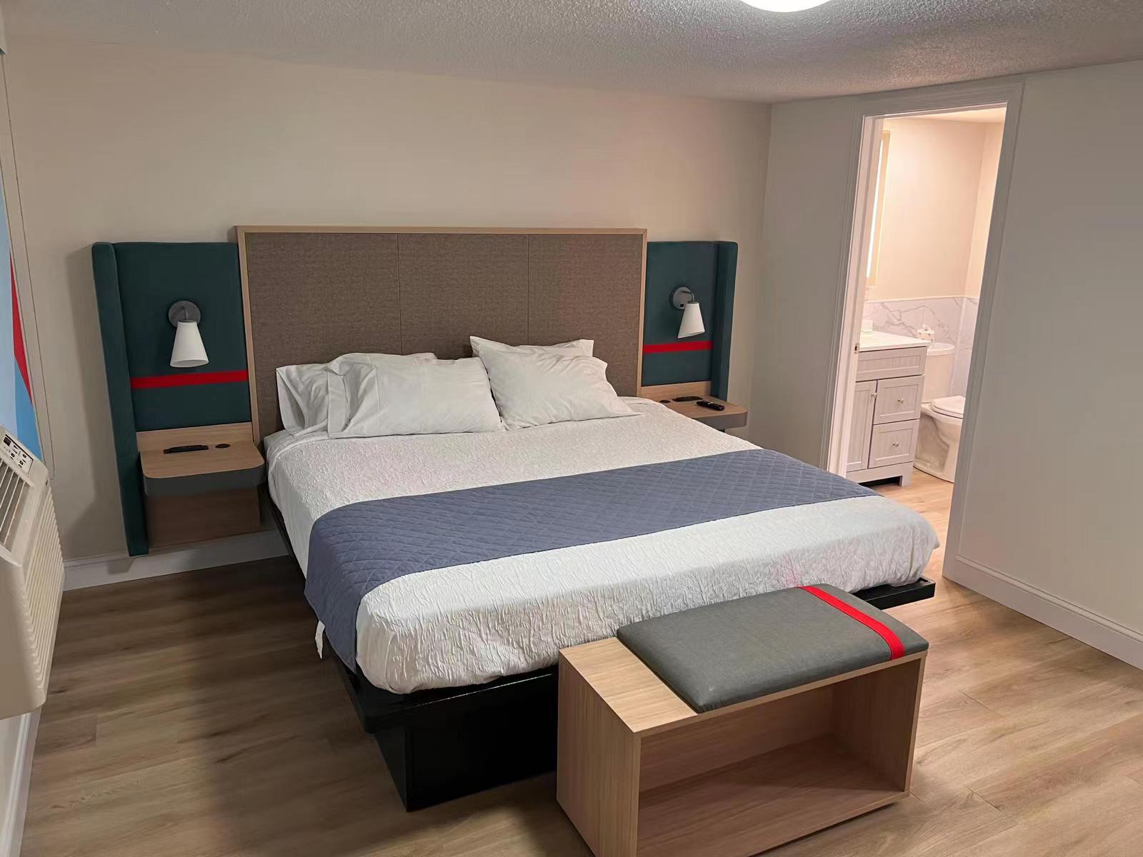 Finished guestroom installation of Avid Hotels King suite furniture package, including headboard, bed base, and luggage bench by Hyman Hospitality.