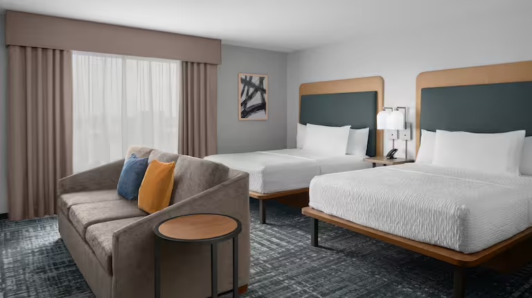 Application view of Homewood Suites GR-323 furniture in an open-plan studio suite with two queen beds and an integrated seating area.
