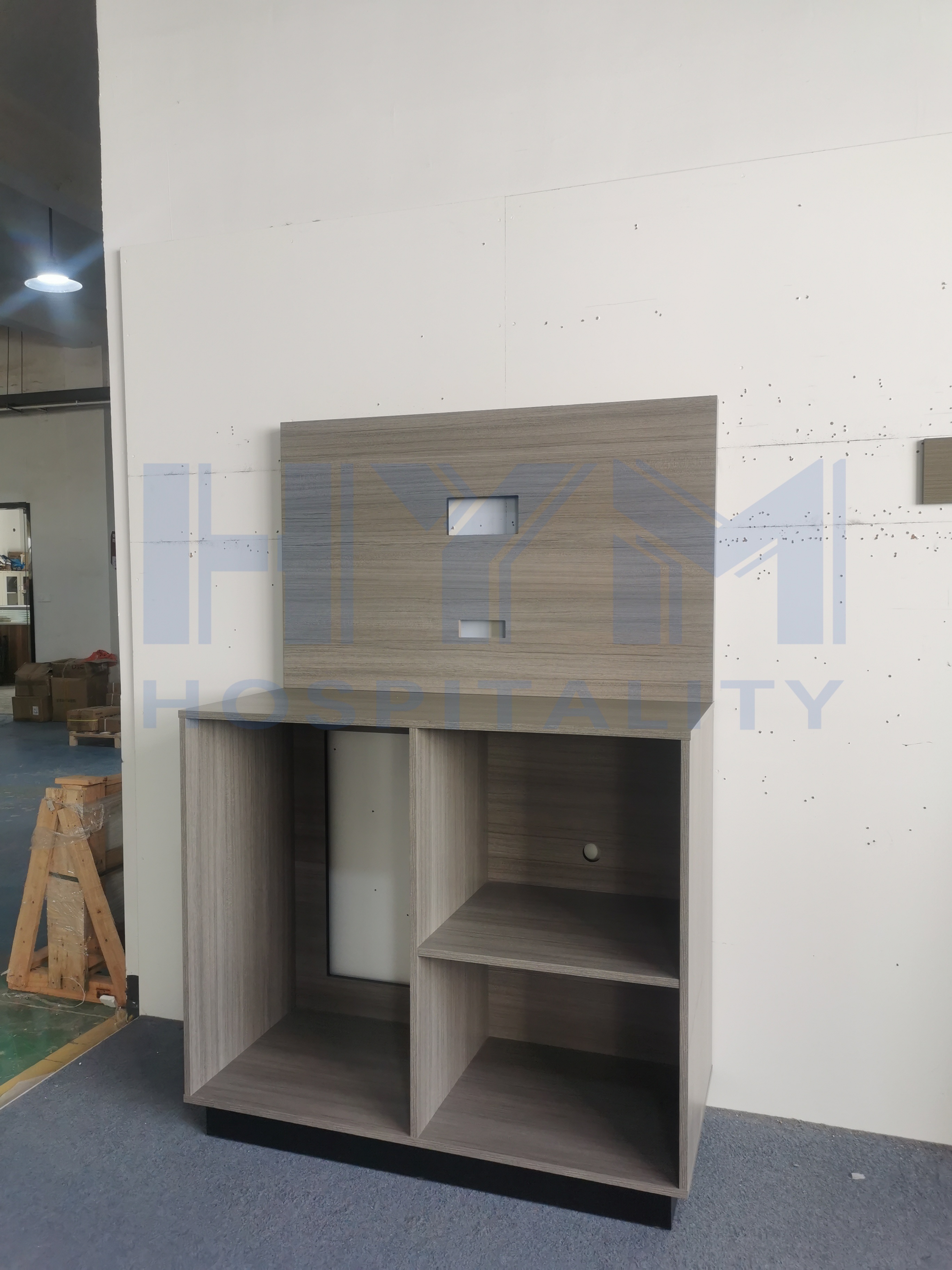 GR-311 grey oak hotel TV stand front-left view with open storage compartment and shelves, factory floor background